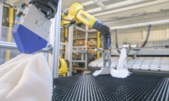 Yellow robotic gripper arms holding towels in a laundry facility with IDS industrial cameras.